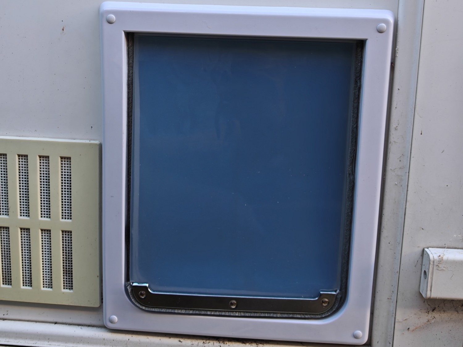 A dog flap fitted into the lower panel of a white uPVC door, beside an air vent