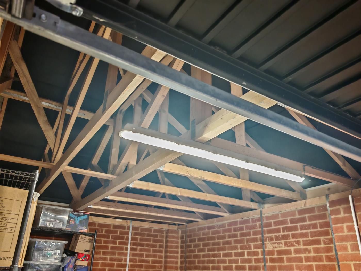 Wide view of a garage lit by a new LED strip light, showing brick walls and roof trusses