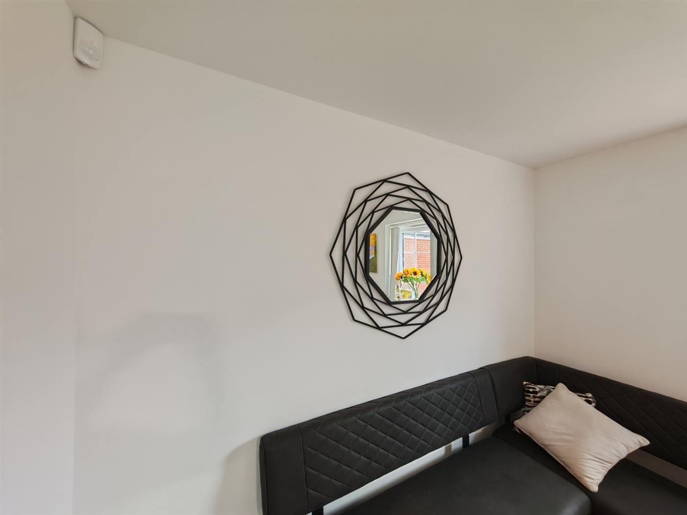 A large geometric black-framed mirror hung on a plastered wall above a corner sofa