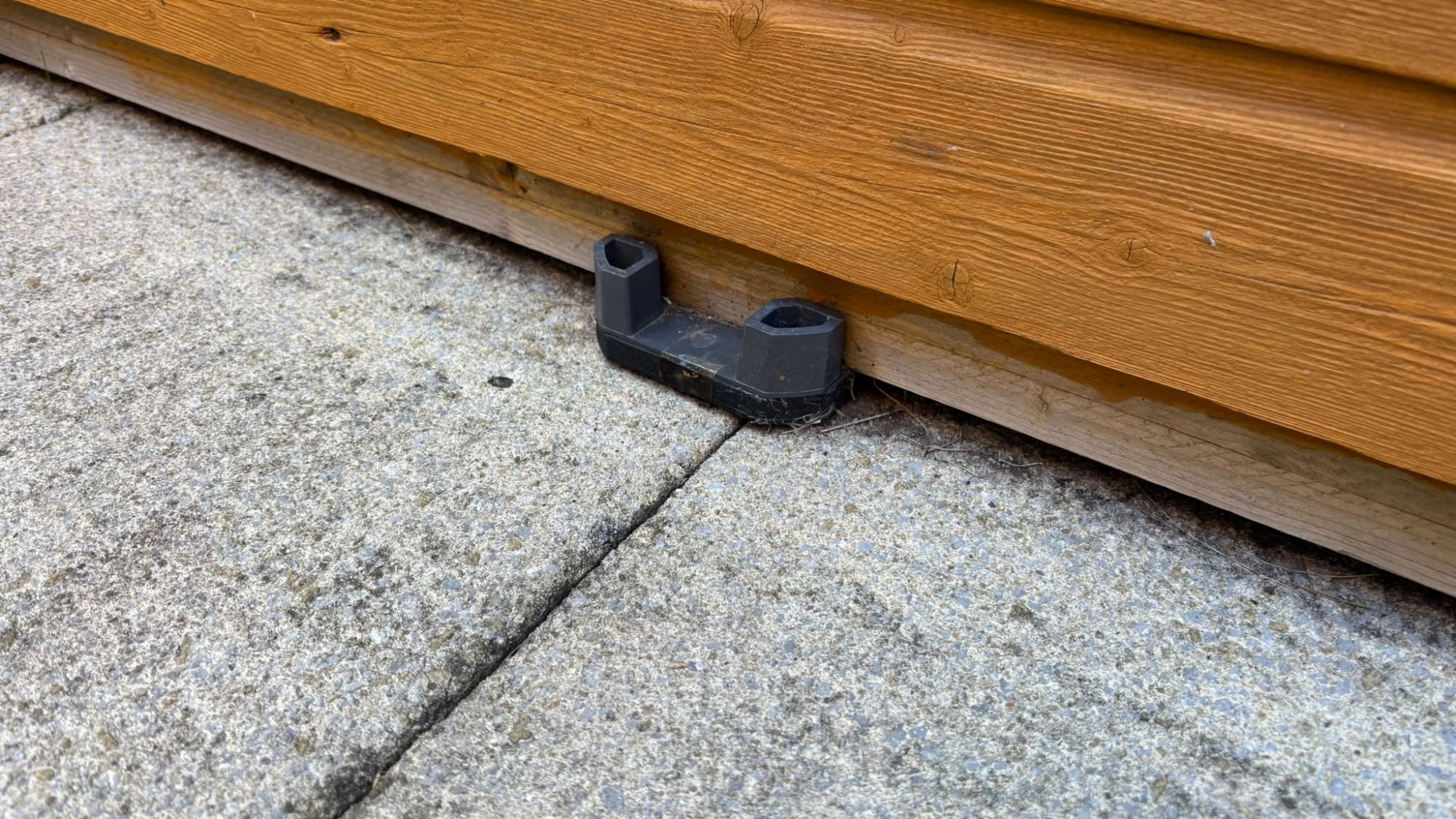 Close-up of a black plastic spacer holding a timber bearer off the paving