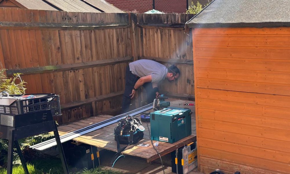 Spiros leaning over the shed floor with a track saw, tools and cases around him, beside the orange shed
