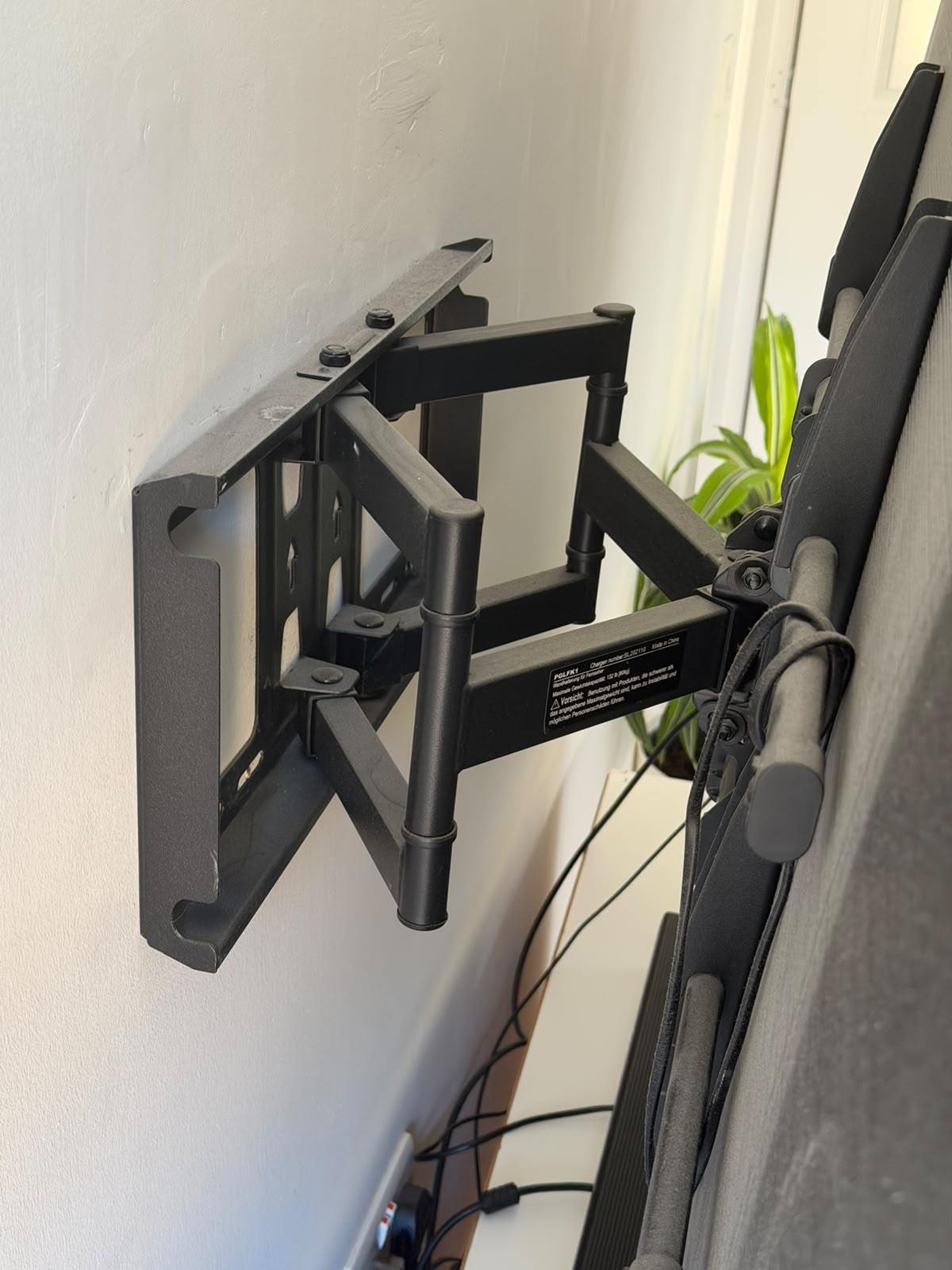 A full-motion television bracket fixed to the wall with the arm extended, showing the wall plate and fixings