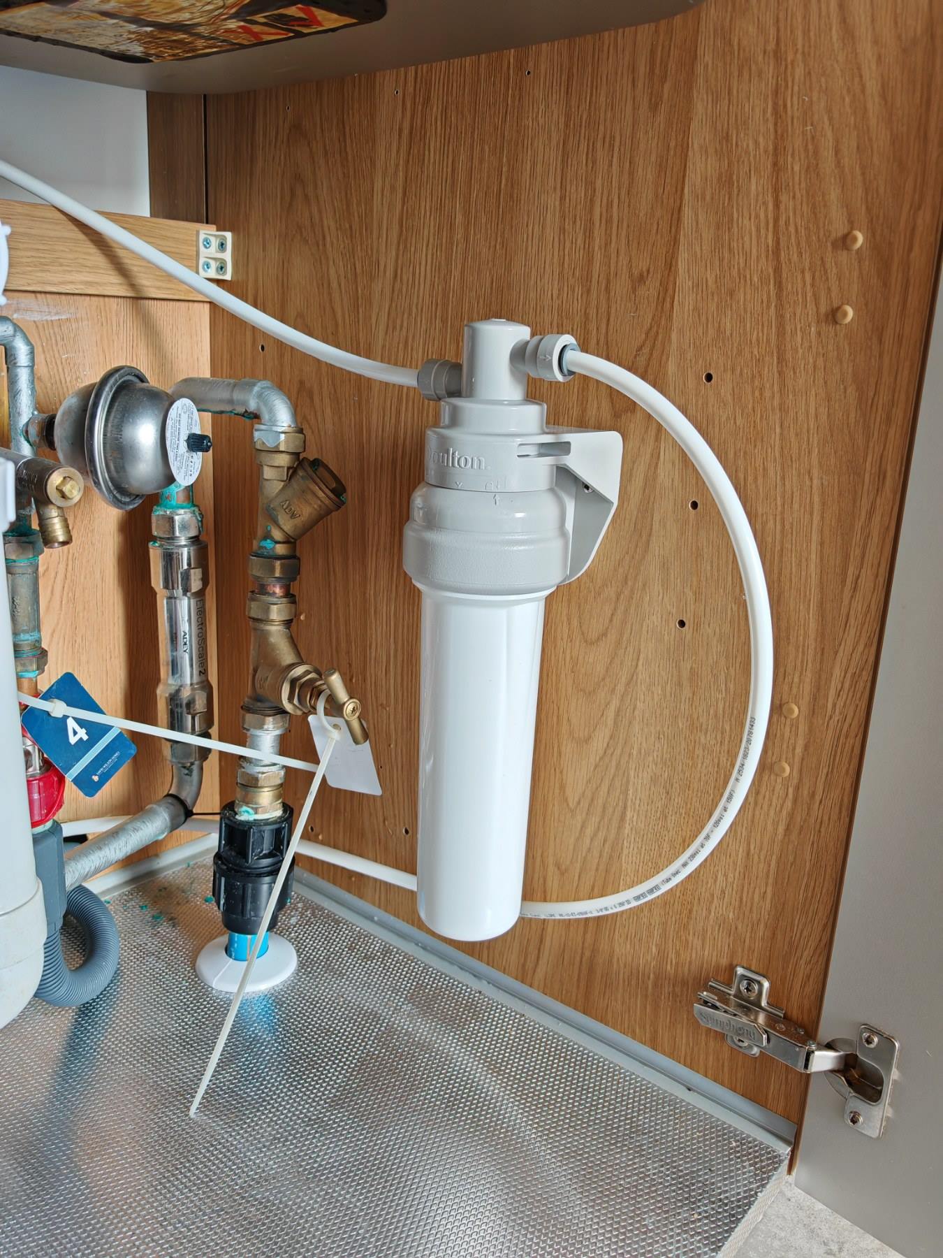 An under-sink water filter housing plumbed in neatly inside a kitchen cupboard